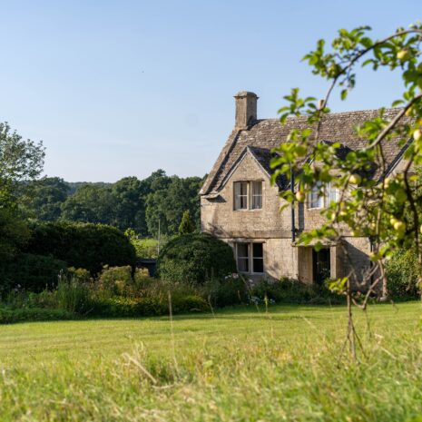 A stone brick house surrounded by green grass and trees with blue skies